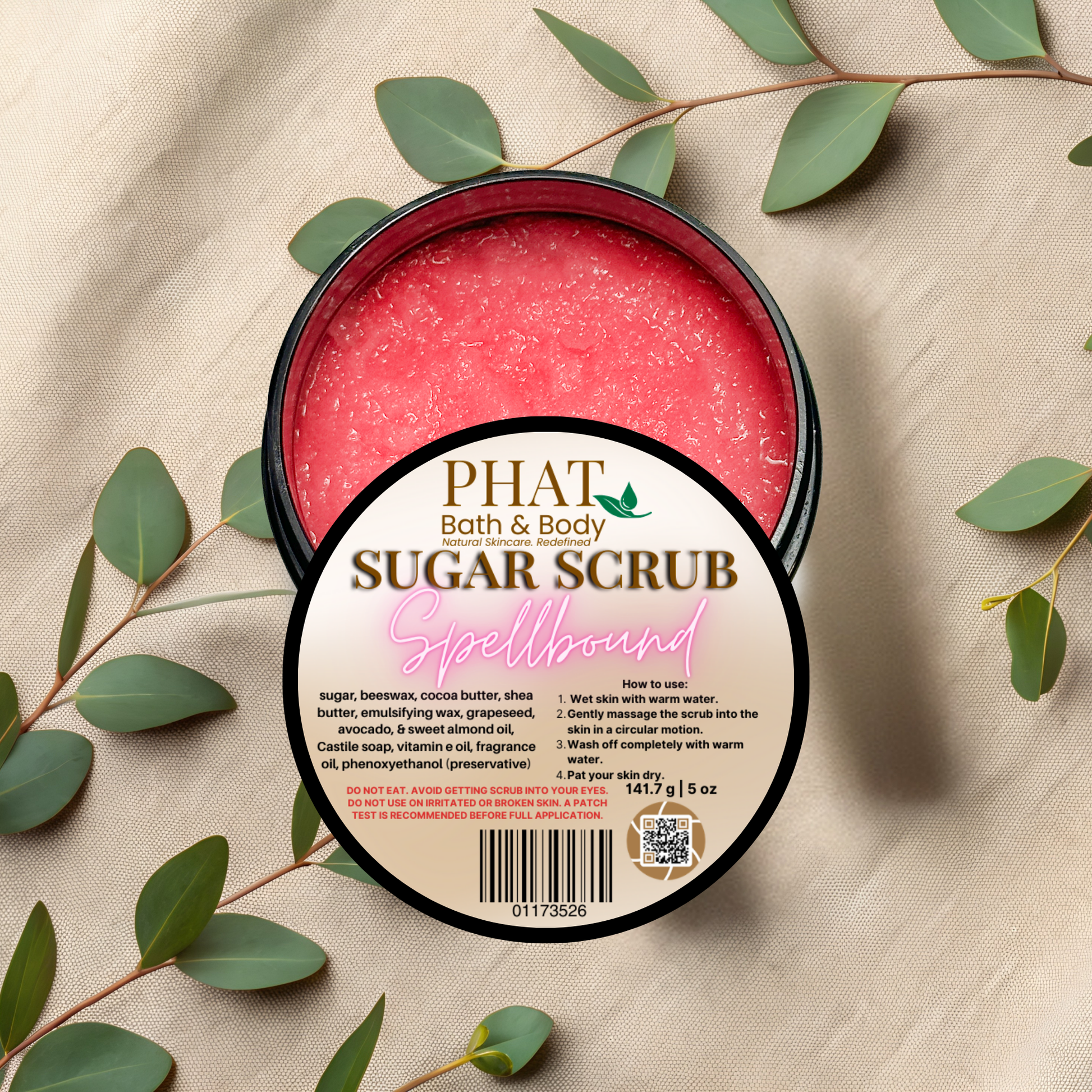 PHAT Bath & Body sugar scrub container with green leaves on a beige fabric background