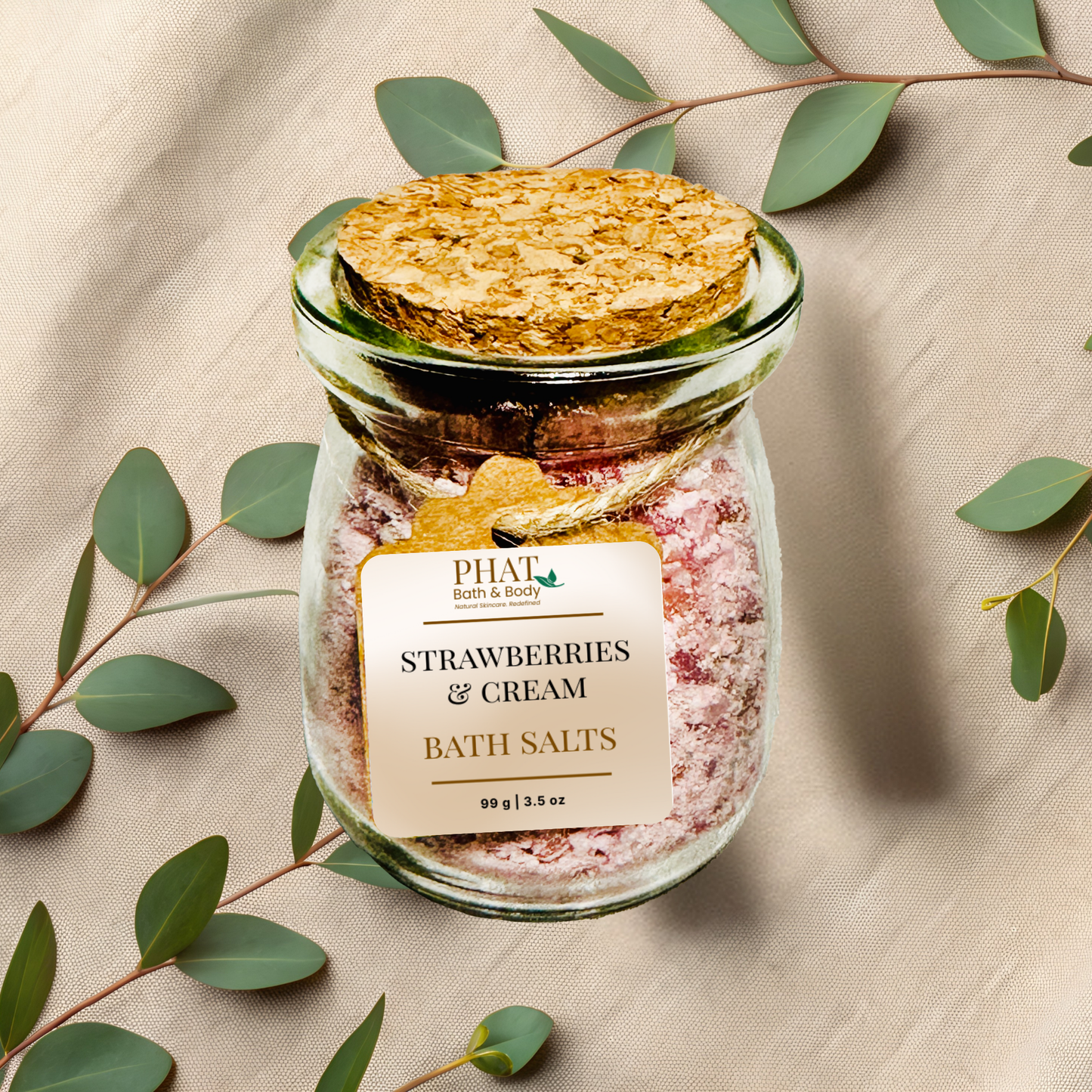 Jar of 'strawberry' bath salts with a cork lid on a beige fabric background with eucalyptus leaves.