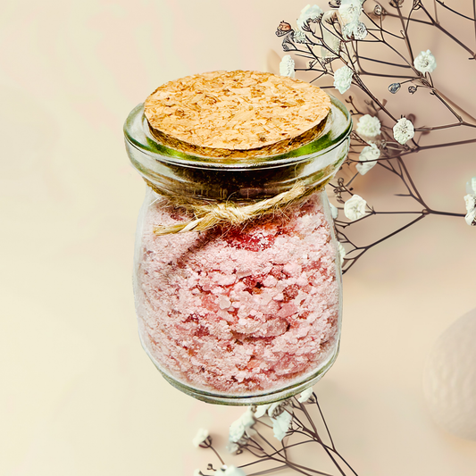 Glass jar with pink bath salt and a wooden lid on a light background