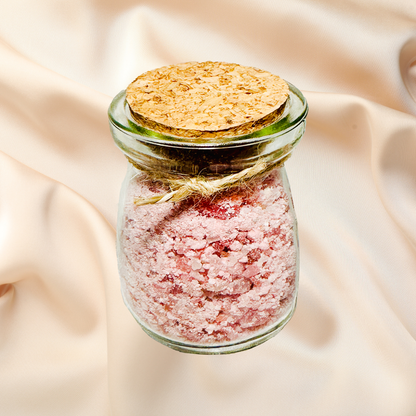 Glass jar with pink bath salts and cork lid on a soft beige fabric background