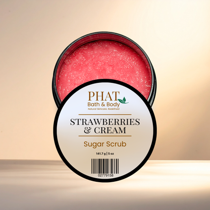 An open round tub of PHAT Bath & Body Strawberry & Cream Sugar Scrub, showing the pinkish-red scrub inside, with the front label facing forward on a warm beige background.