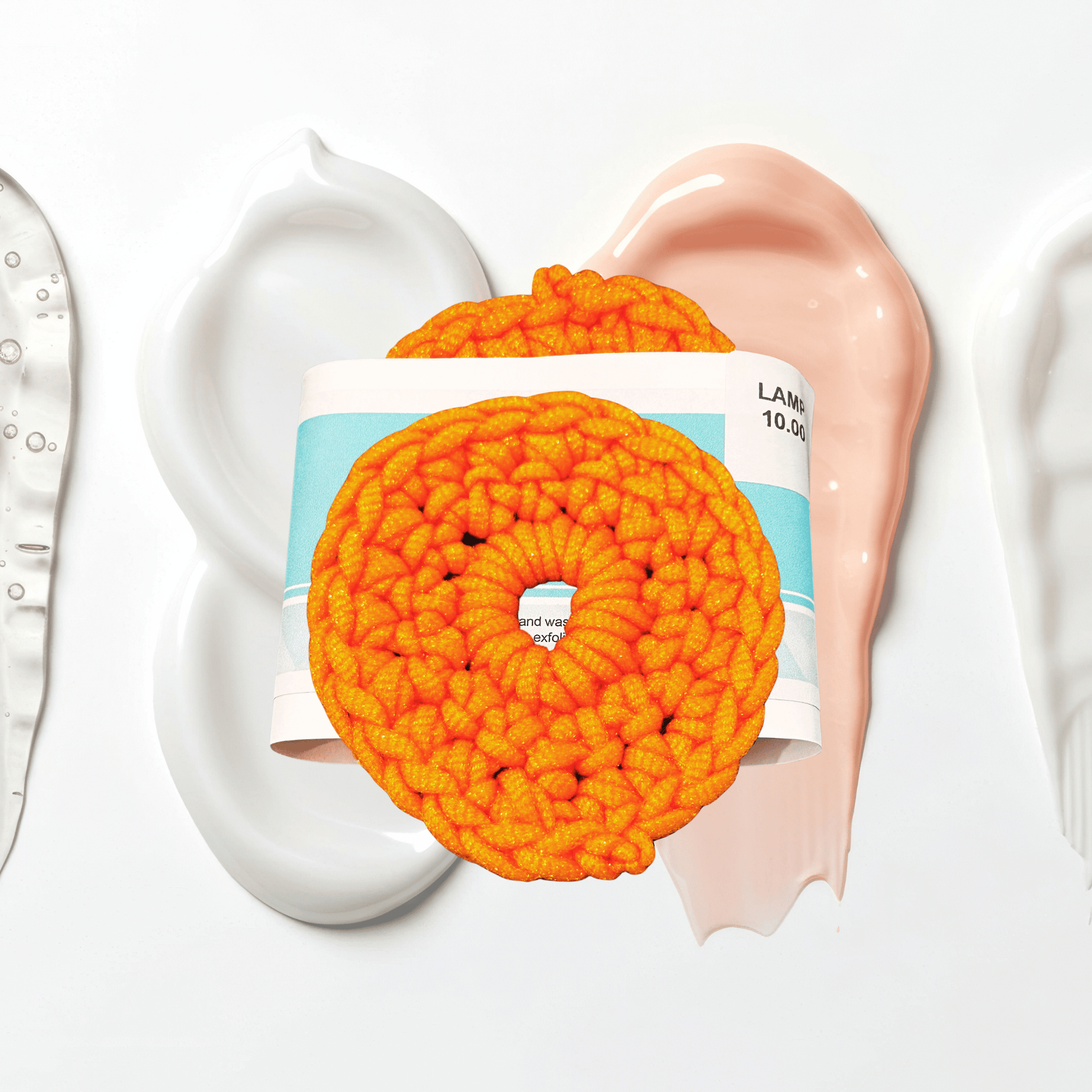 Orange crocheted scrubbie with a product container on a white background