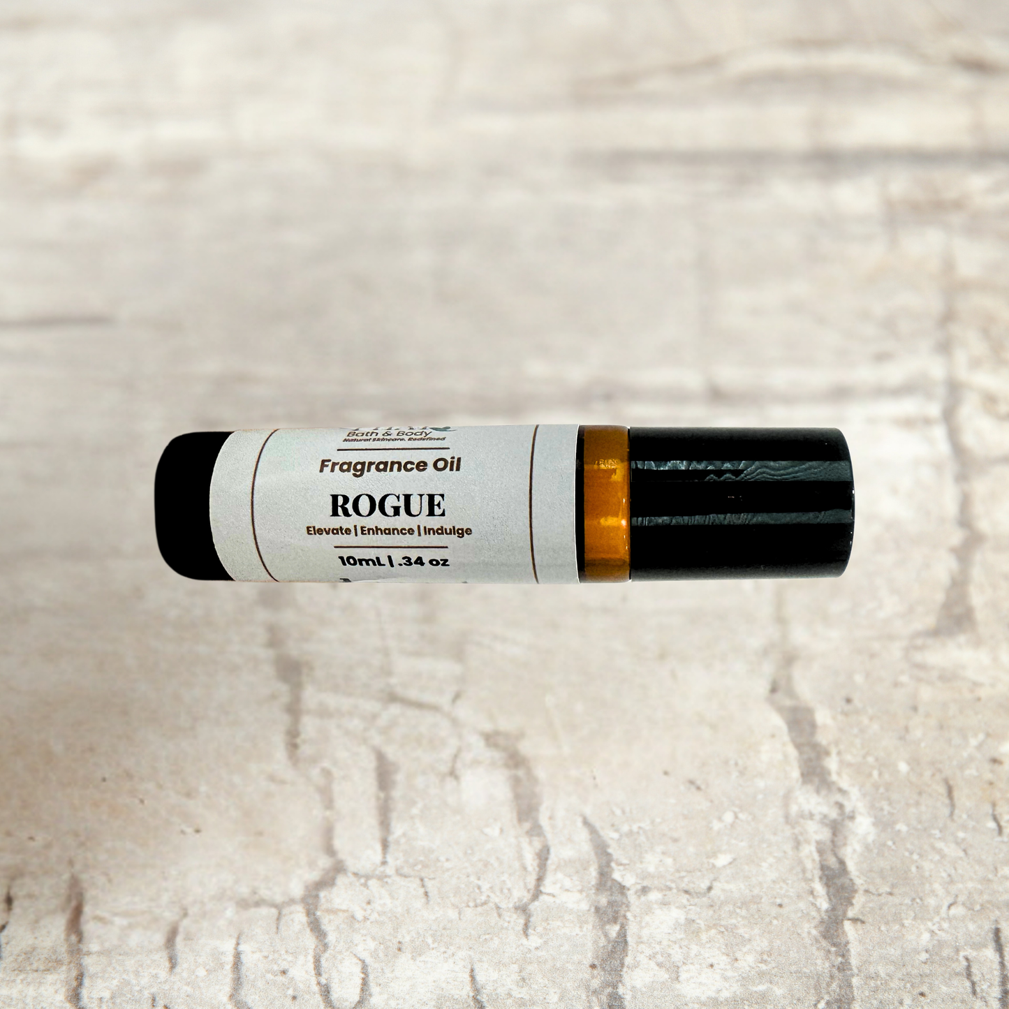 A 10ml tube of Rogue Fragrance Oil decant fragrance, featuring a white label with black text and a black cap, resting horizontally on a light beige stone-textured background.