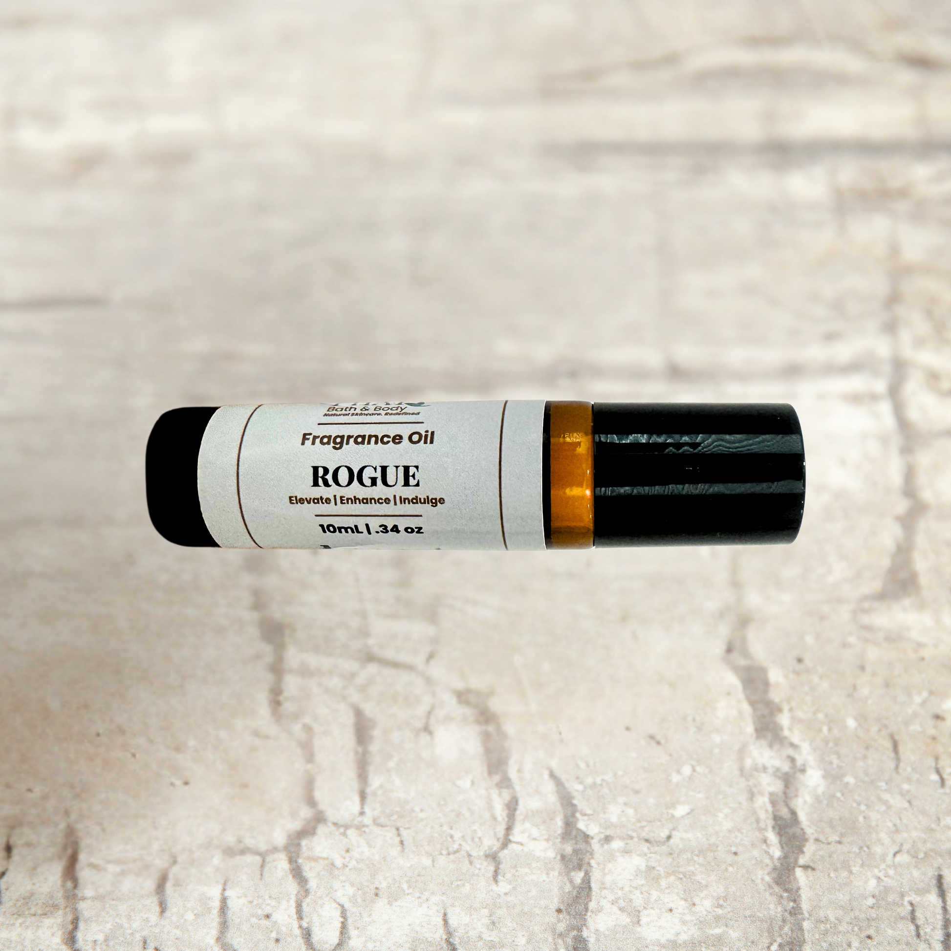 A 10ml tube of Rogue Fragrance Oil decant fragrance, featuring a white label with black text and a black cap, resting horizontally on a light beige stone-textured background.