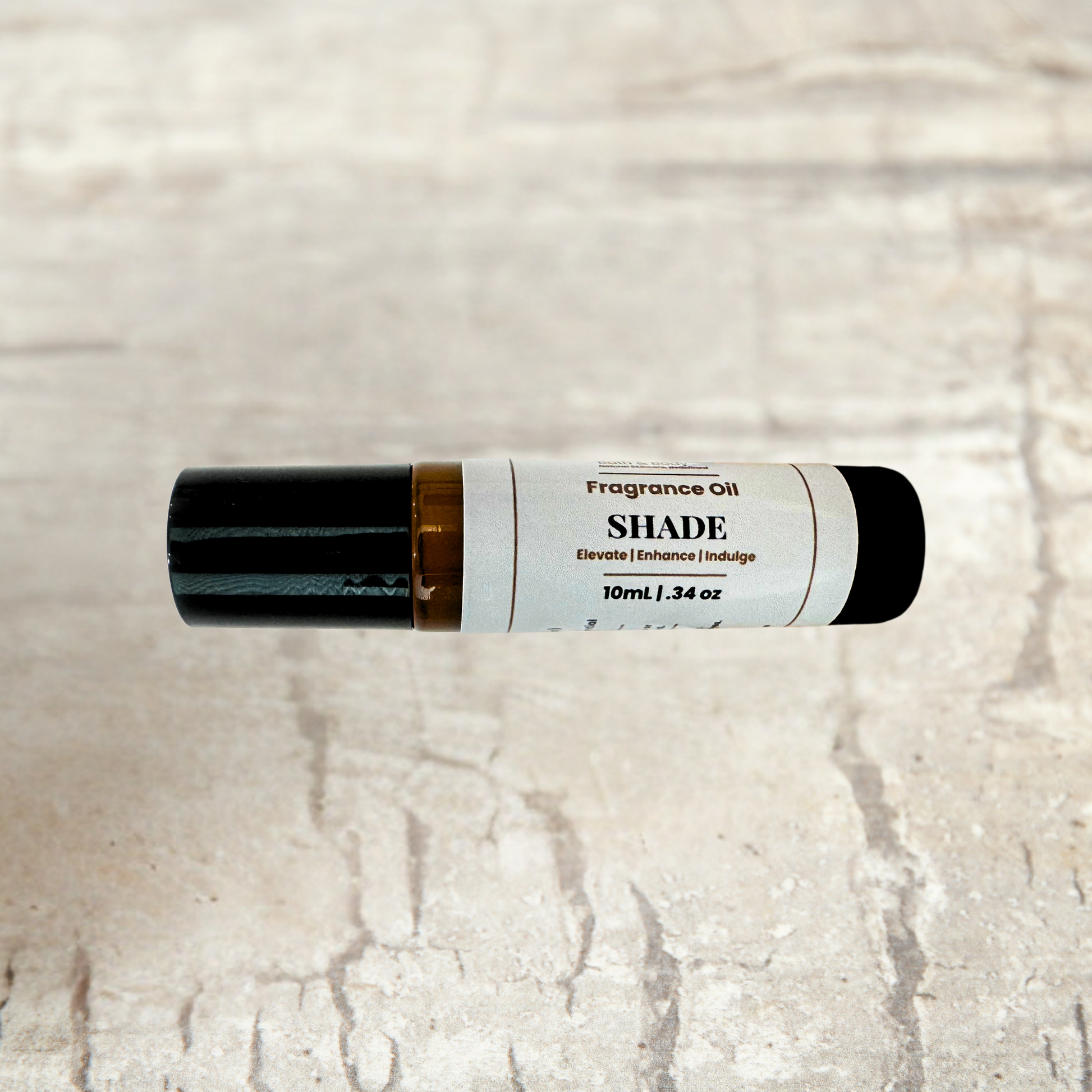 A 10ml roll-on bottle of SHADE Fragrance Oil, featuring a white label with black text and a black cap, resting horizontally on a light beige stone-textured background.