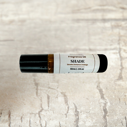 A 10ml roll-on bottle of SHADE Fragrance Oil, featuring a white label with black text and a black cap, resting horizontally on a light beige stone-textured background.