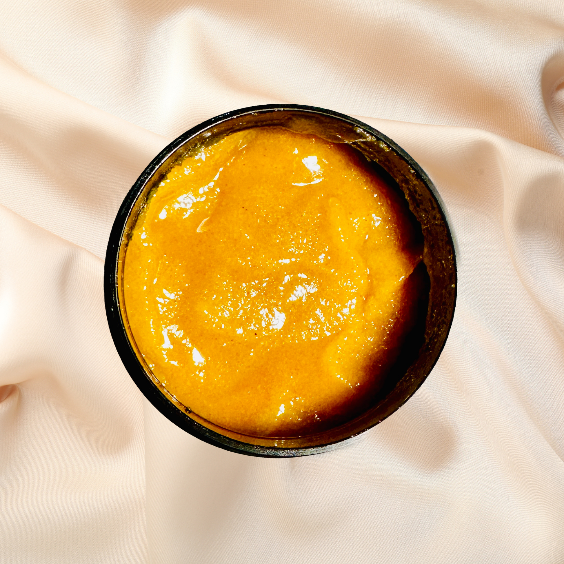 Yellowish-brown scrub in a black container on a beige fabric background