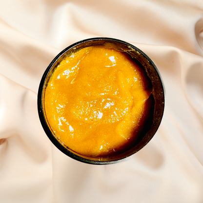 Yellowish-brown scrub in a black container on a beige fabric background
