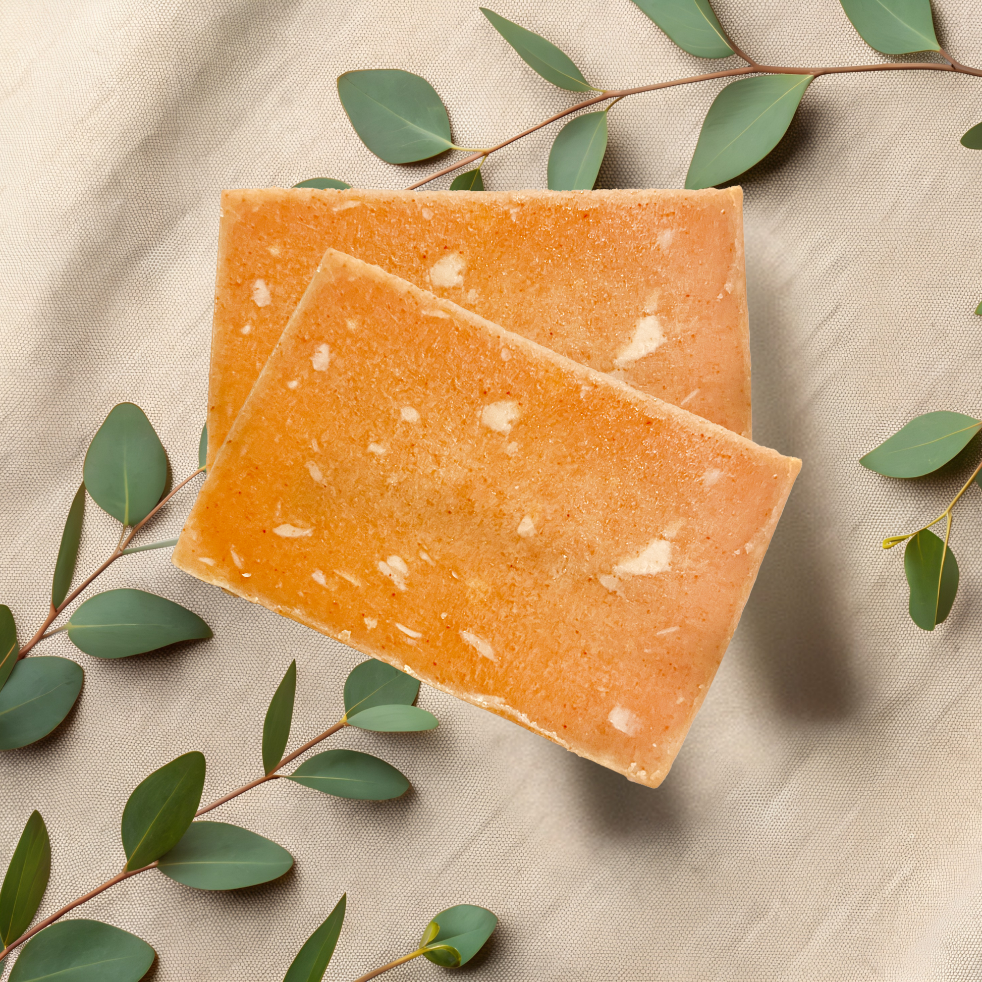 Two orange soap bars on a beige fabric background with green leaves.