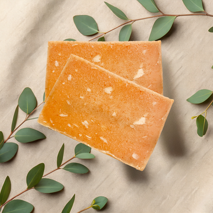 Two orange soap bars on a beige fabric background with green leaves.