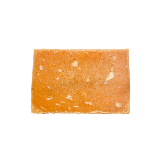 Rectangular piece of orange-colored soap with white specks on a white background