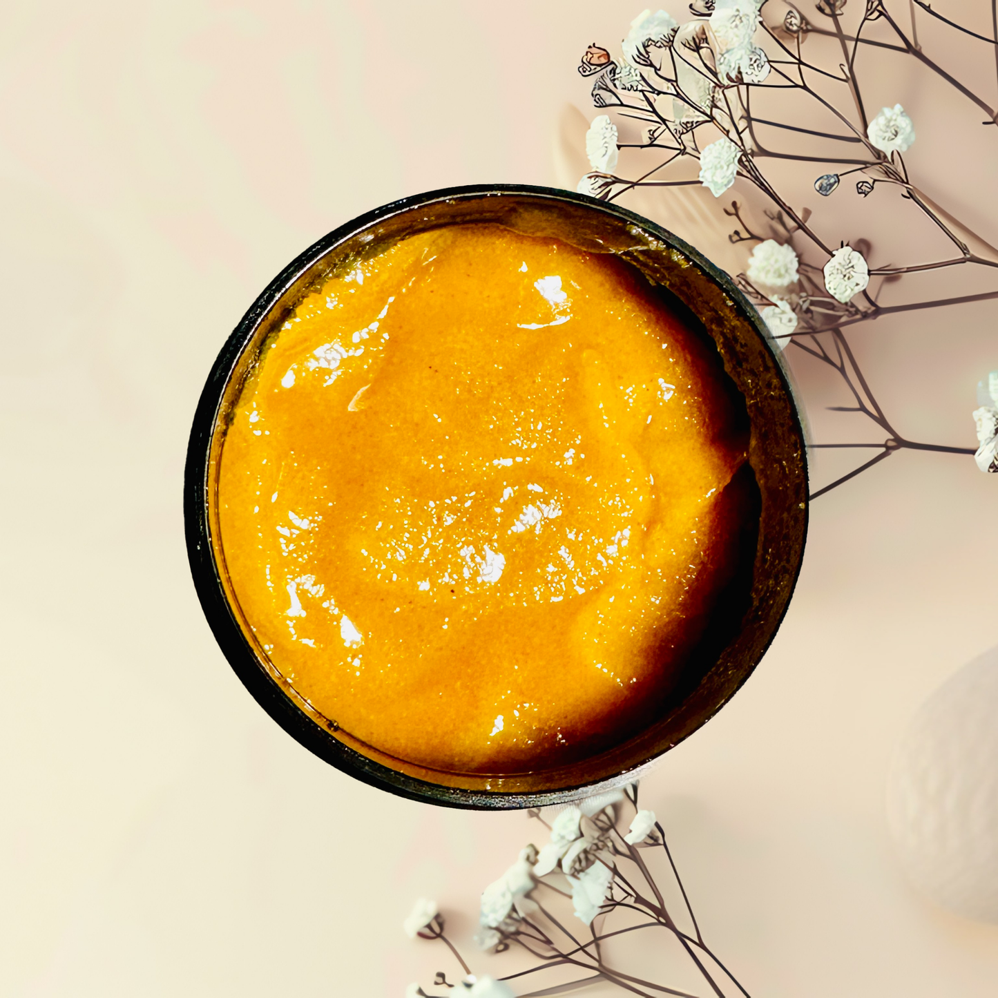 Bowl of orange scrub on a light pink background with white flowers.