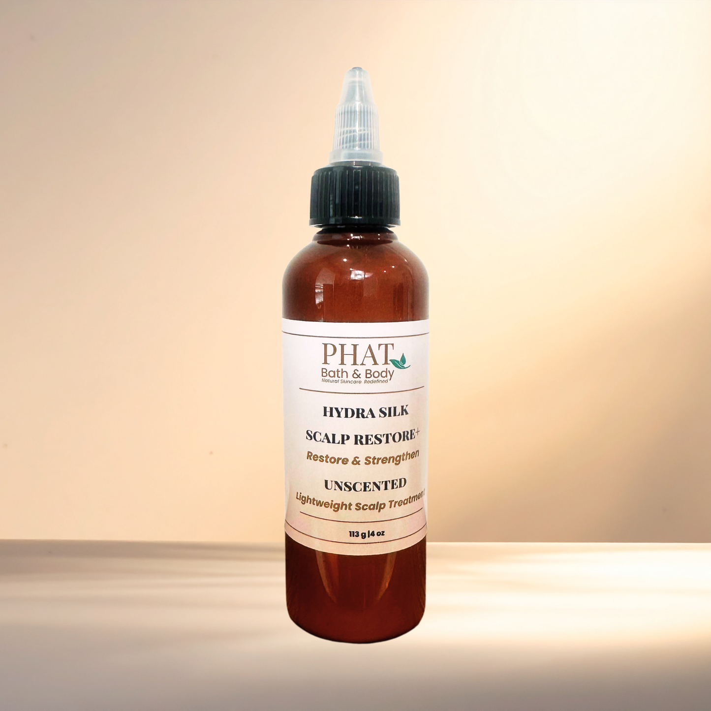 An amber bottle of PHAT Bath & Body Hydra Silk Scalp Restore Unscented treatment with a black cap and white label, set against a warm beige gradient background.