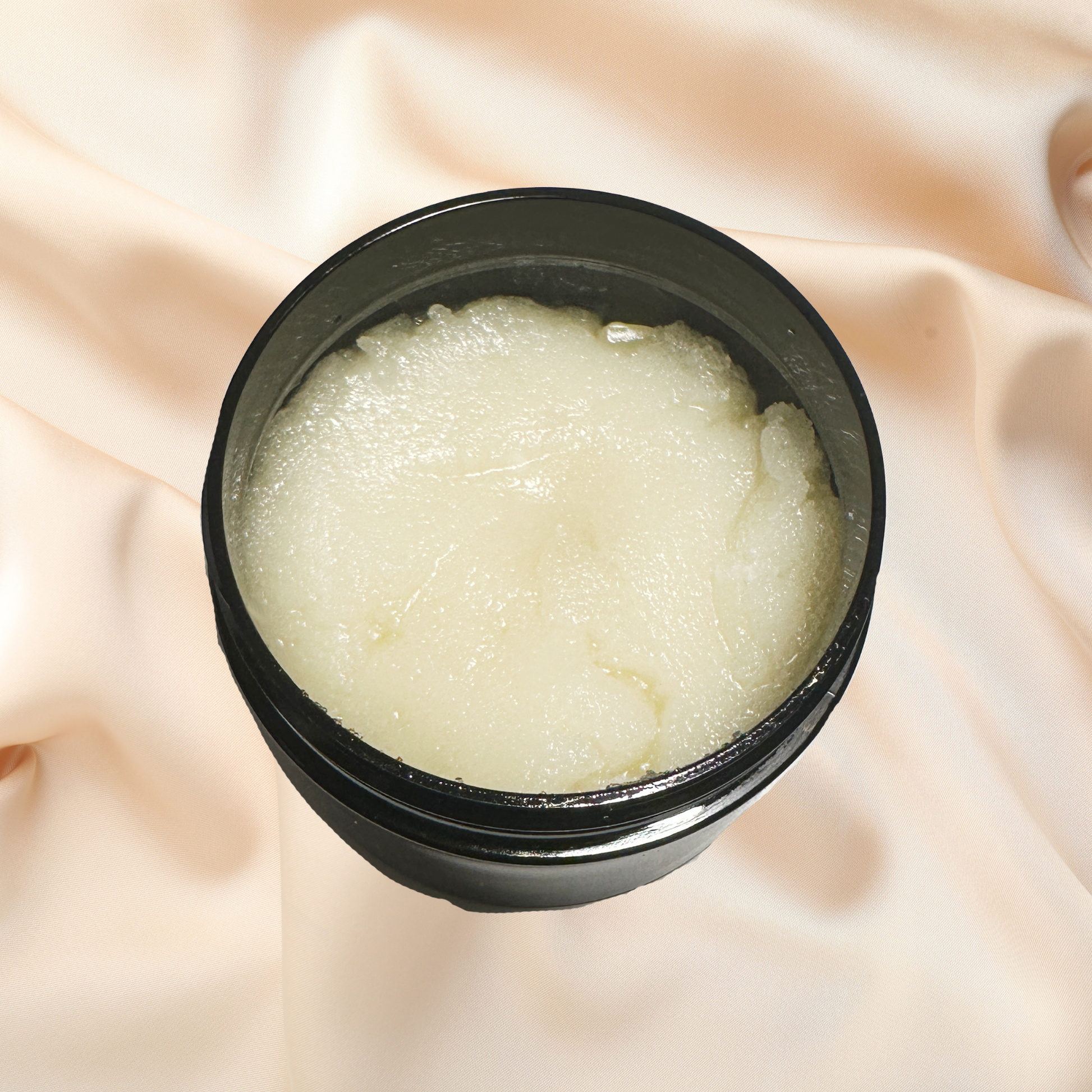Black container of white scrub on a soft pink fabric background