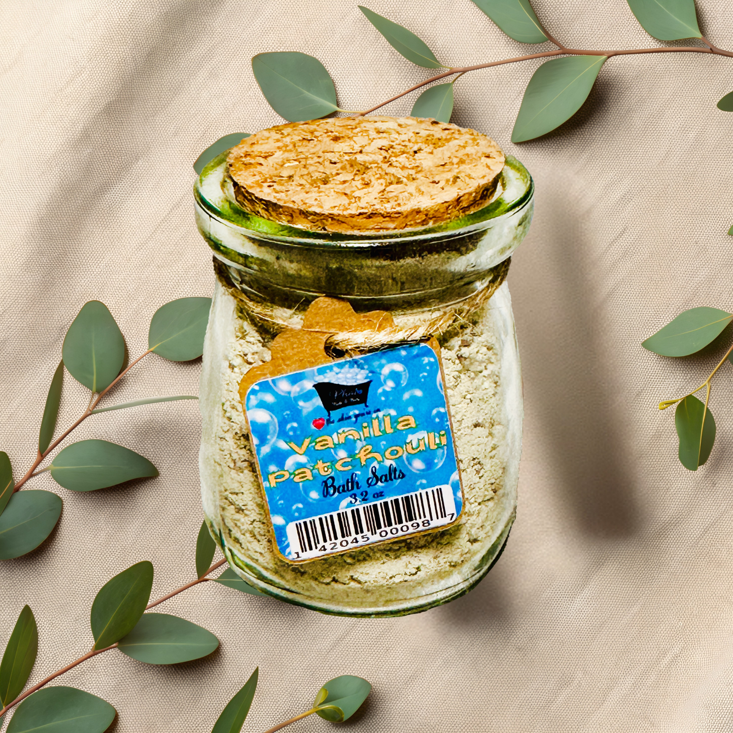 Jar of vanilla patchouli bath salts with a label on a beige fabric background with green leaves.