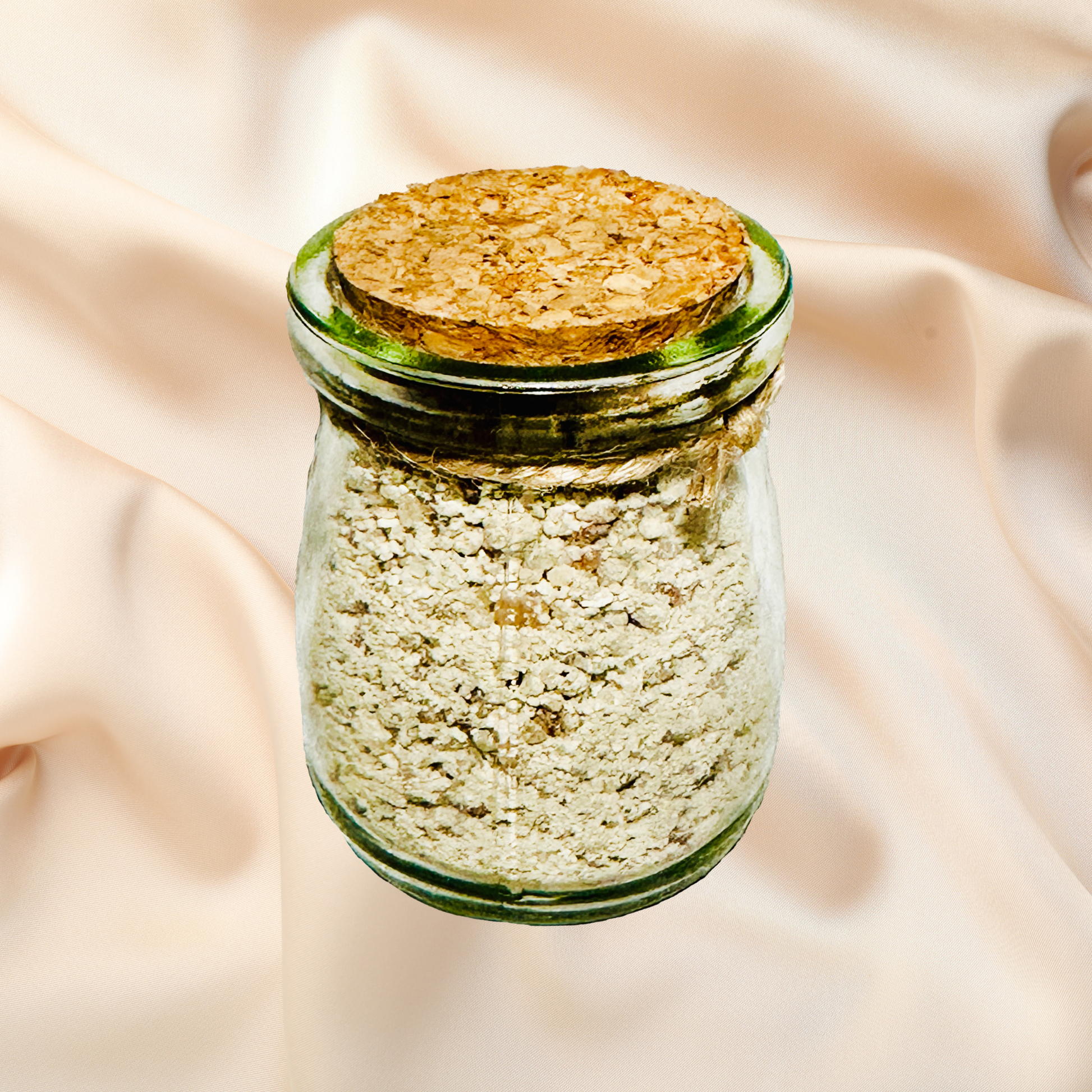 Glass jar with cork lid containing a light-colored bath salts on a beige fabric background