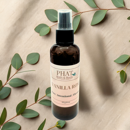 Bottle of 'Vanilla Rose' spray from Phat Bath & Body on a beige fabric background with green leaves.