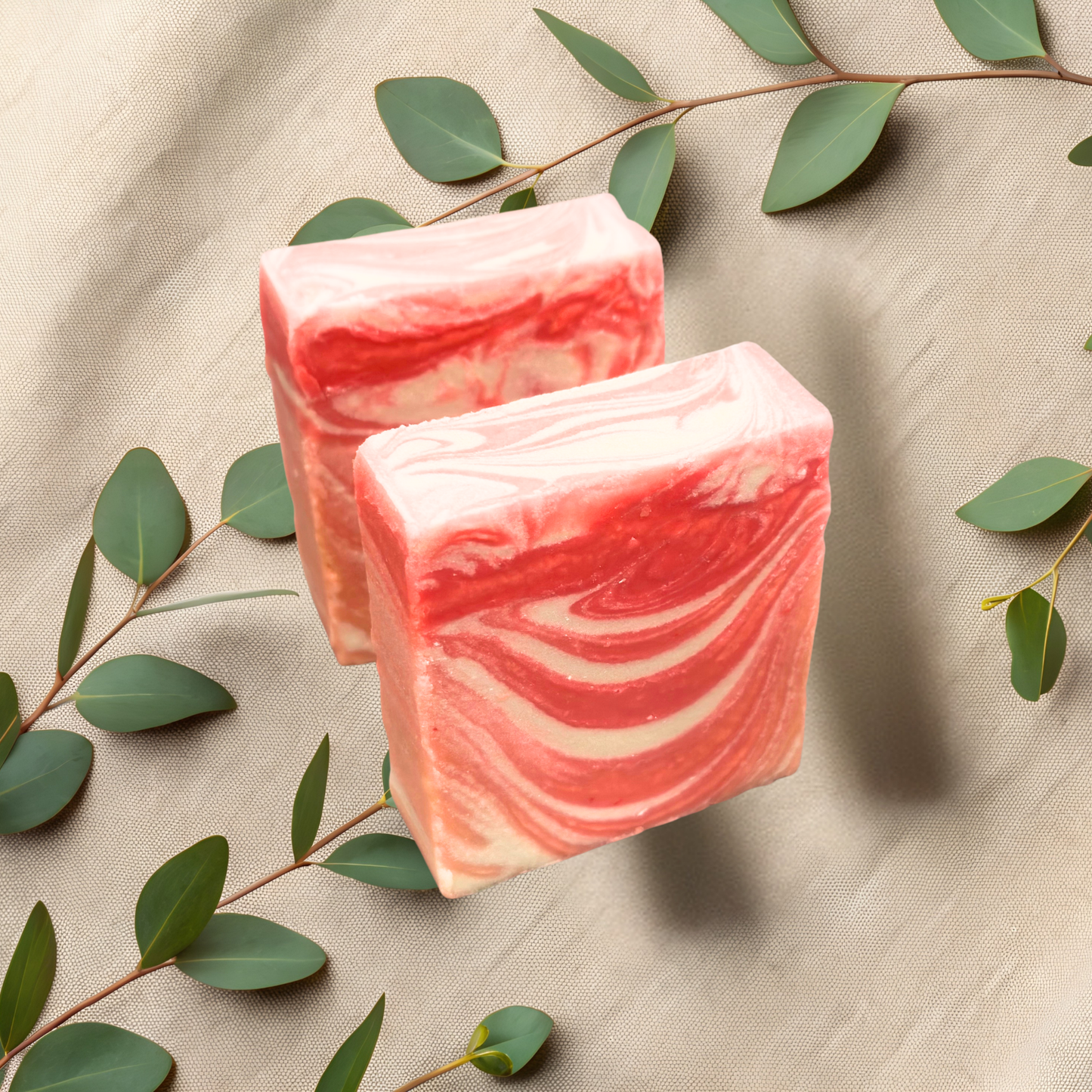 Two pink marbled soap bars on a beige fabric background with green leaves.