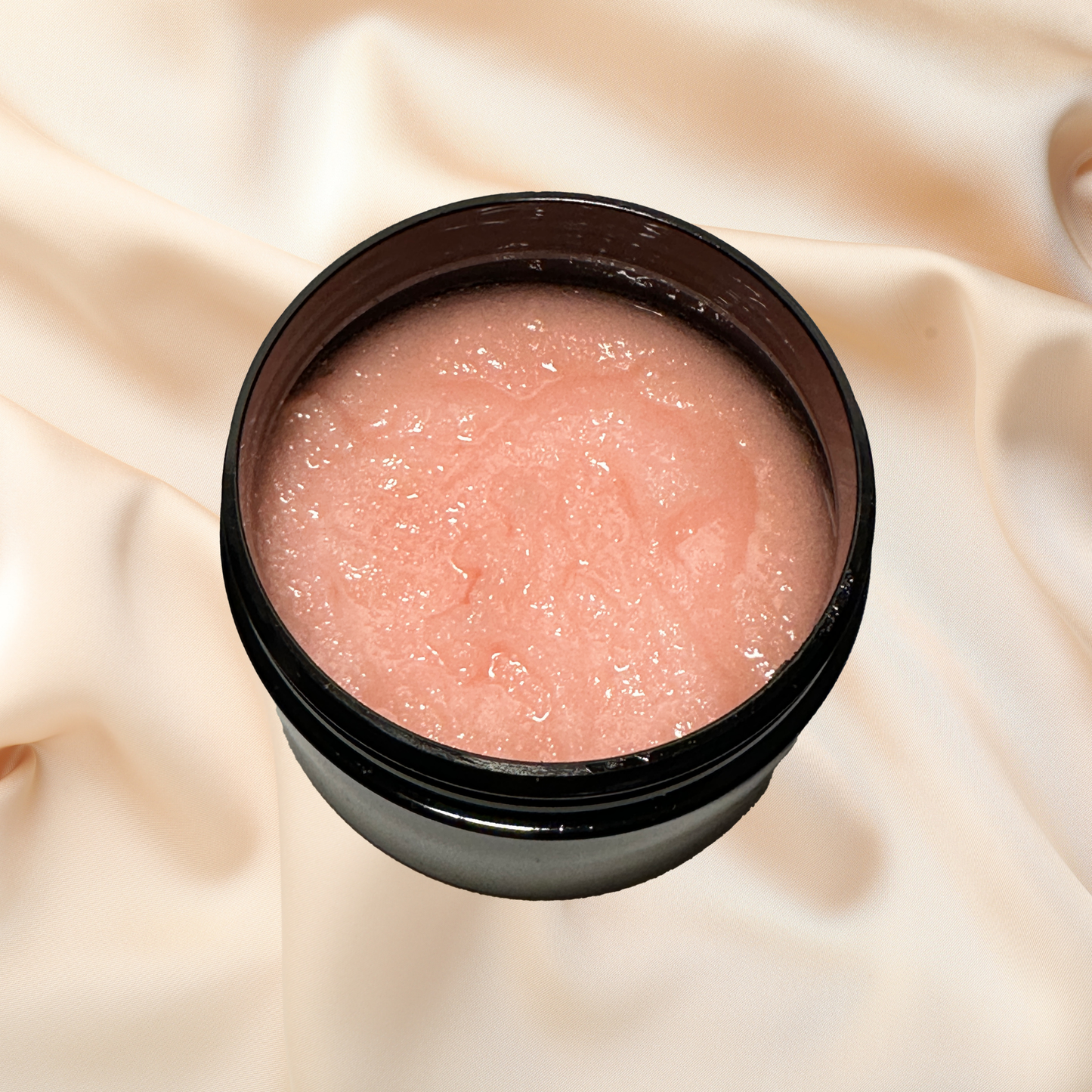 Pink sugar scrub in a black container on a beige fabric background