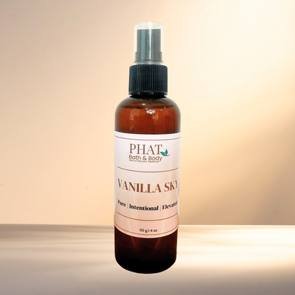 An amber glass spray bottle of PHAT Bath & Body Vanilla Sky with a black spray cap and a white label, set against a warm beige gradient background.