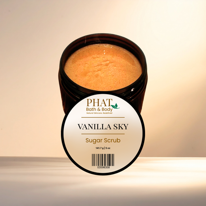 An open jar of PHAT Bath & Body Vanilla Sky Sugar Scrub, showing the light brown scrub inside, with its white and black label in front, set against a warm beige background.