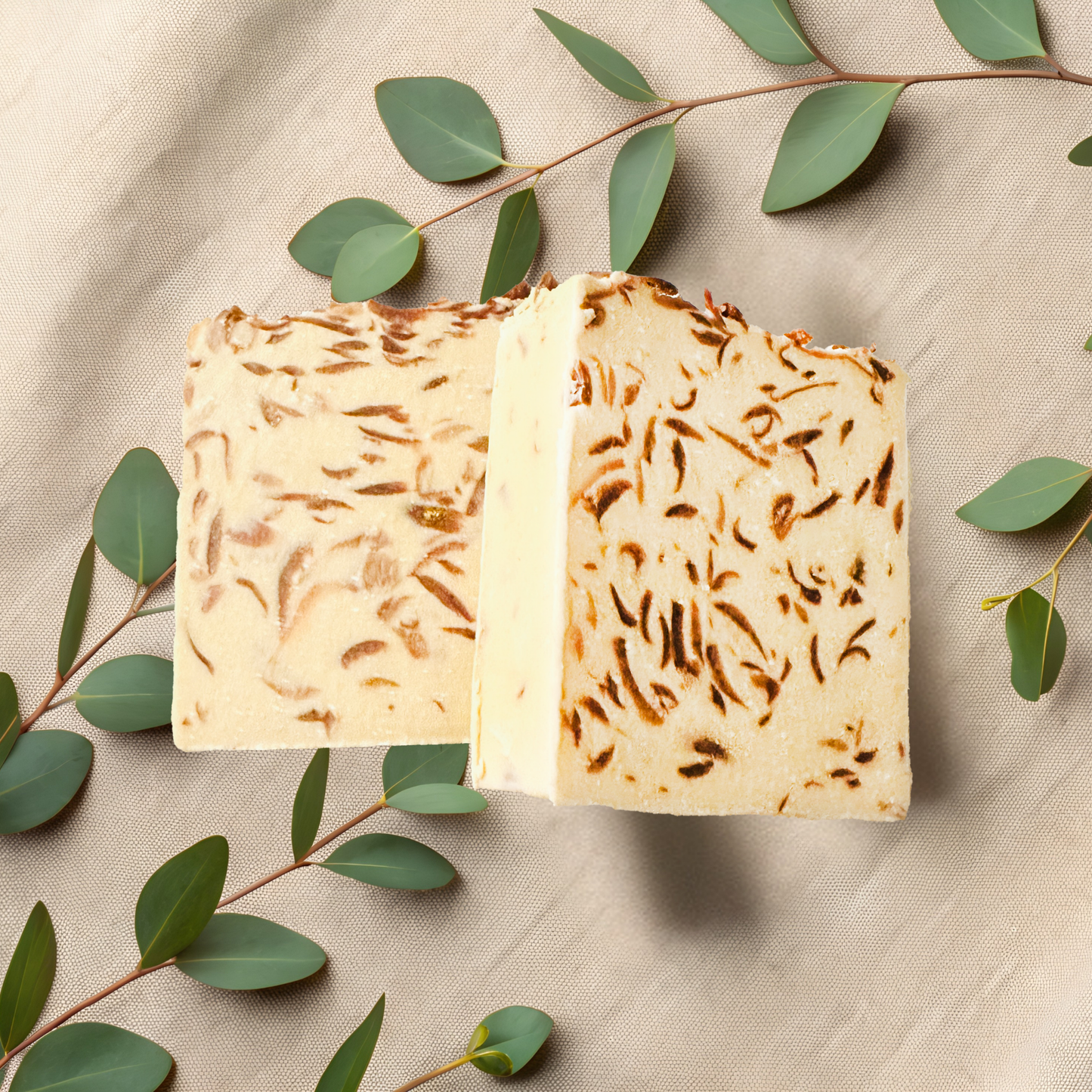 Two pieces of textured soap with green leaves on a beige fabric background
