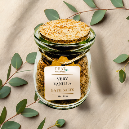 Jar of very vanilla bath salts with a cork lid on a beige fabric background with eucalyptus leaves.