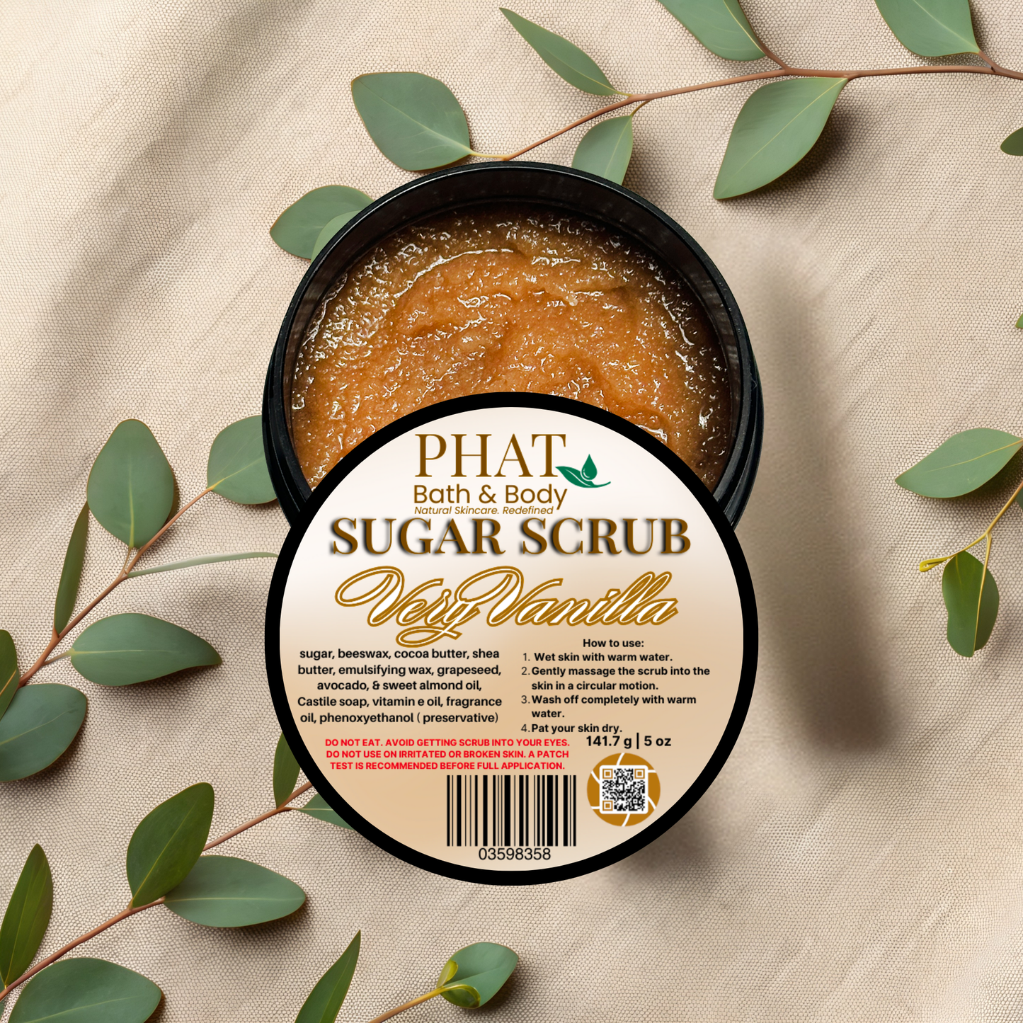 Container of Phat Bath & Body sugar scrub with vanilla scent on a beige fabric background with green leaves.
