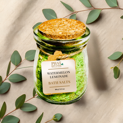 Jar of 'watermelon lemonade Bath Salts' with a cork lid on a beige fabric background with eucalyptus leaves.