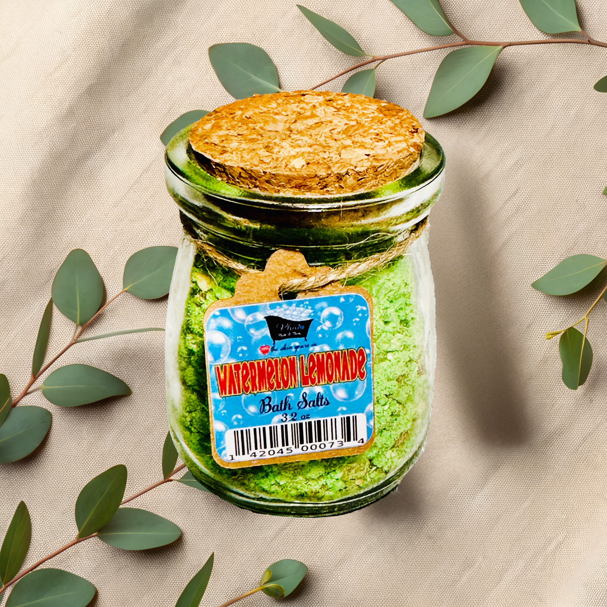 Jar of bath salts with a decorative label on a beige fabric background with green leaves.