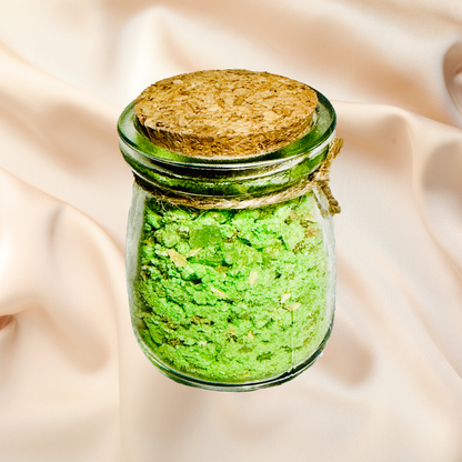 Small glass jar with cork lid containing a green bath salts on a beige fabric background