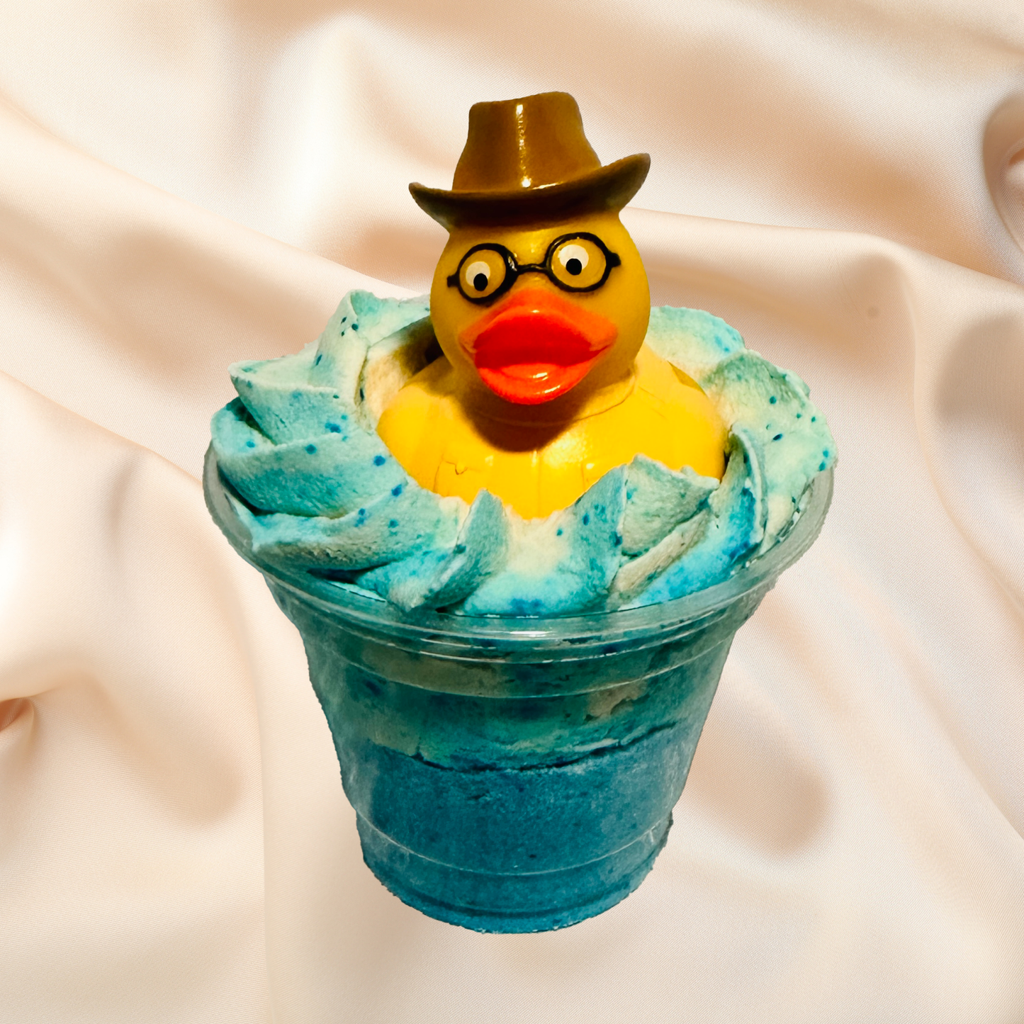 Yellow rubber duck with a hat and glasses in a bubble bomb on a beige fabric background