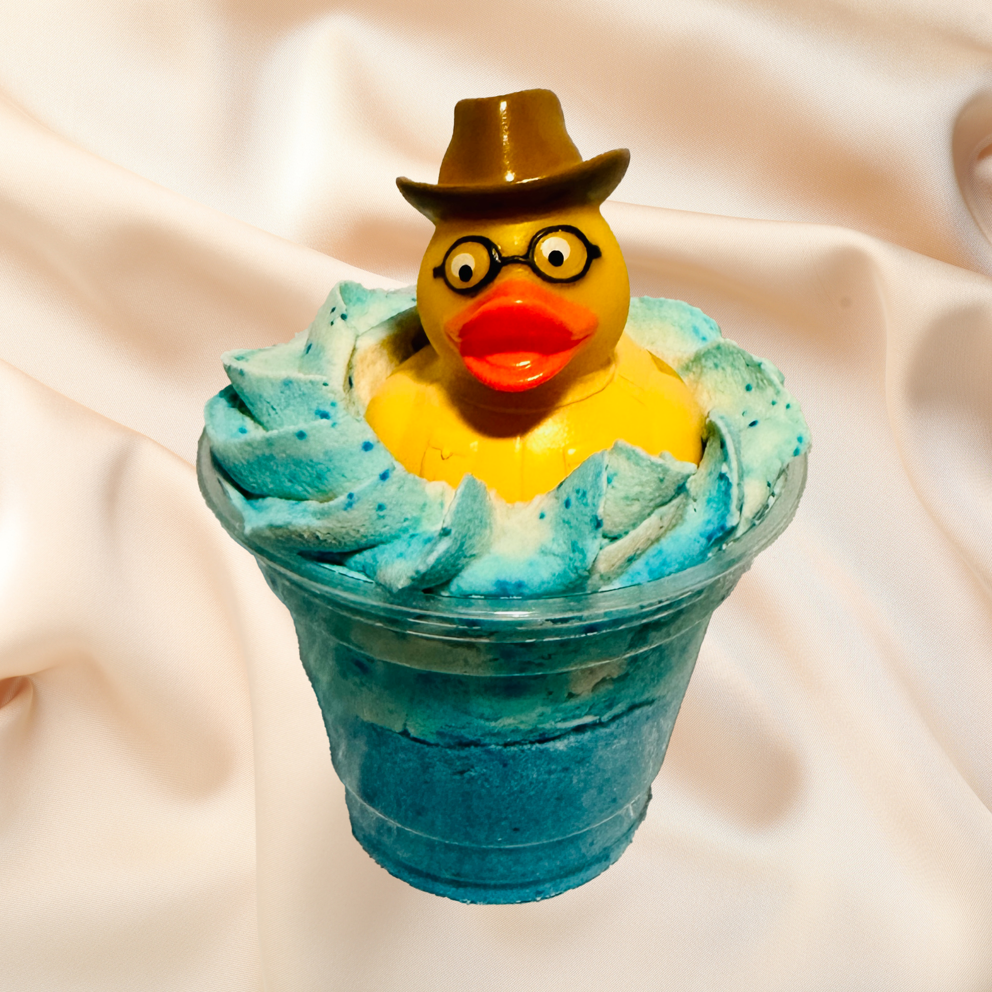 Yellow rubber duck with a hat and glasses in a bubble bomb on a beige fabric background