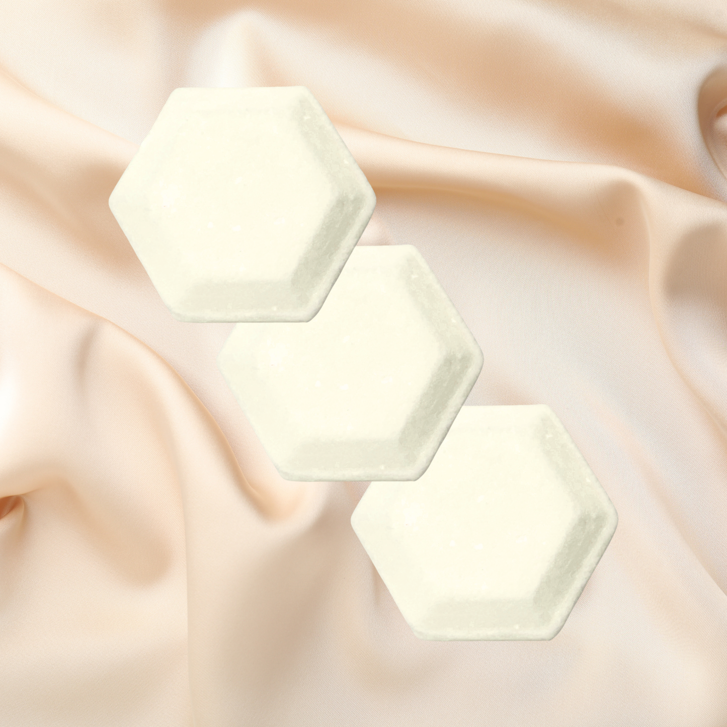 Three hexagonal shower bombs on a soft, draped fabric background