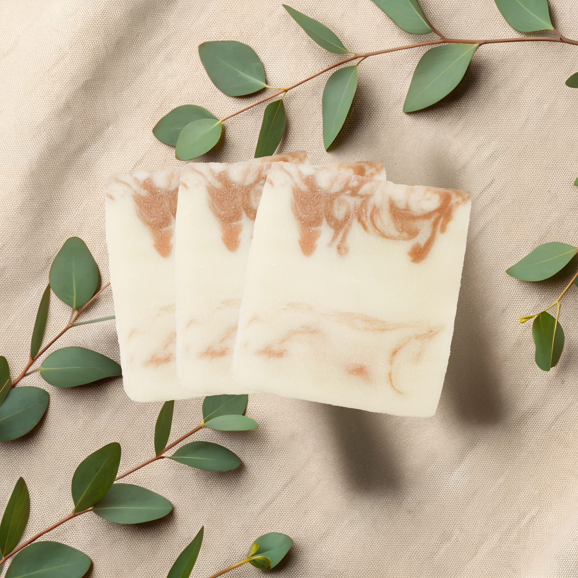 Three marbled soap bars on a beige fabric background with green leaves.