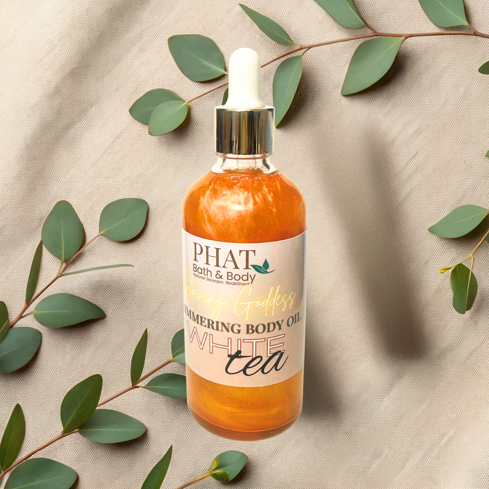 Bottle of Phat Bath & Body White Tea body oil with green leaves on a beige fabric background