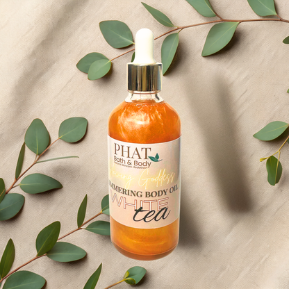 Bottle of Phat Bath & Body White Tea body oil with green leaves on a beige fabric background