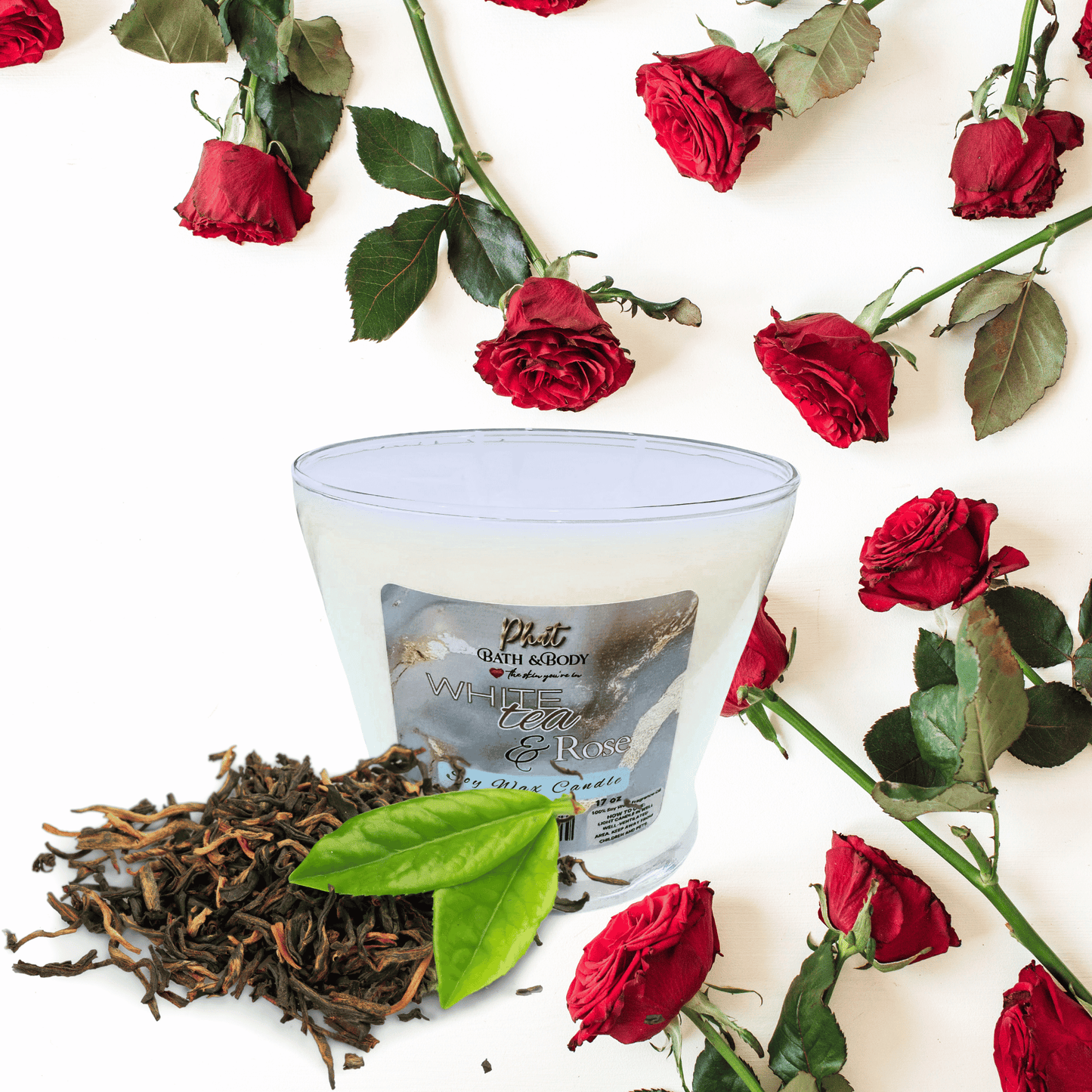 Candle with a label surrounded by red roses and loose tea leaves on a white background