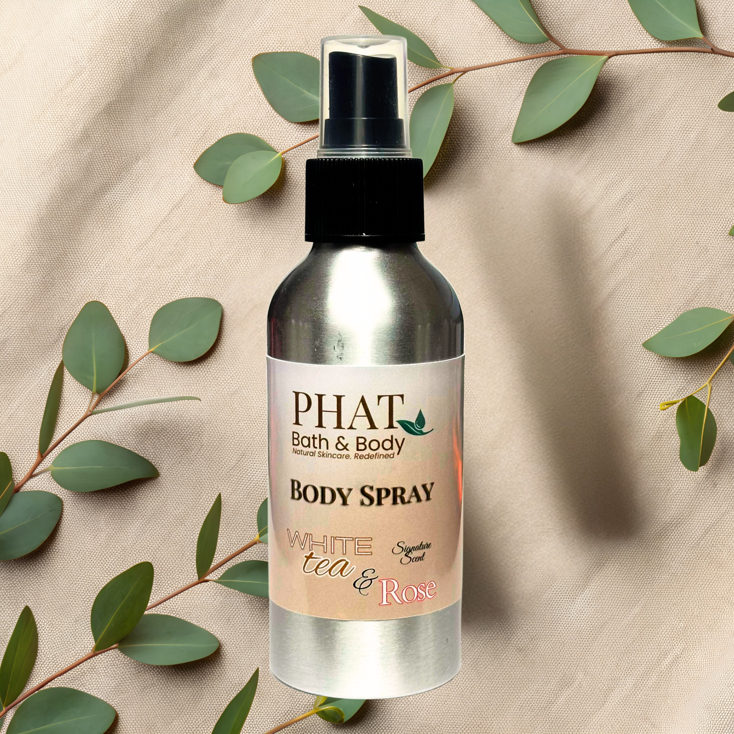 Body spray bottle with 'PHAT Bath & Body' label on a beige fabric background with green leaves.