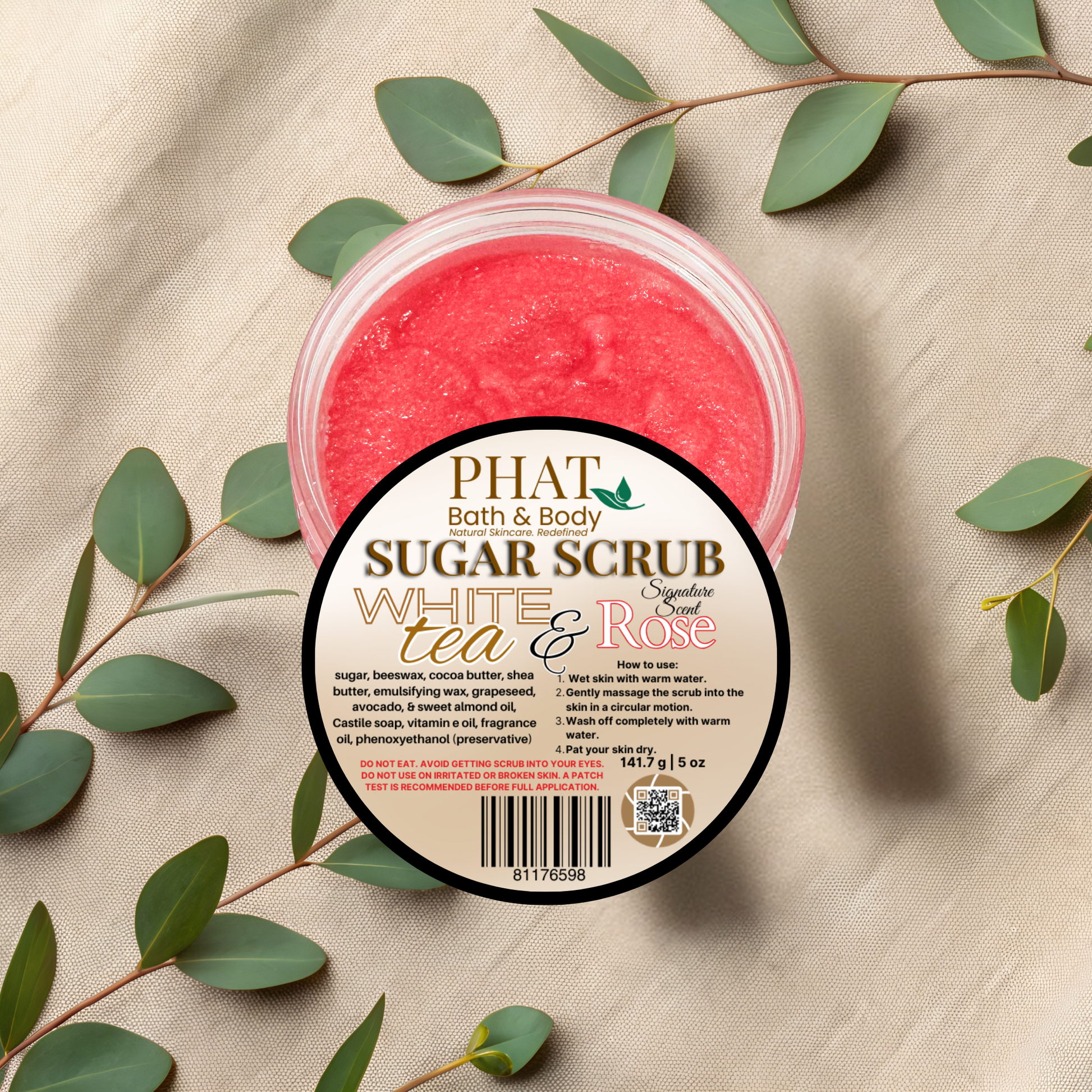 Jar of Phat Bath & Body sugar scrub with green leaves on a beige fabric background