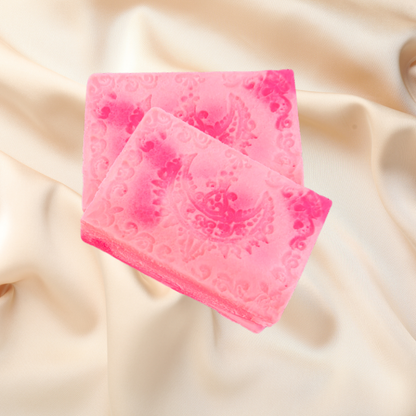 Two pink textured soap bars on a beige fabric background