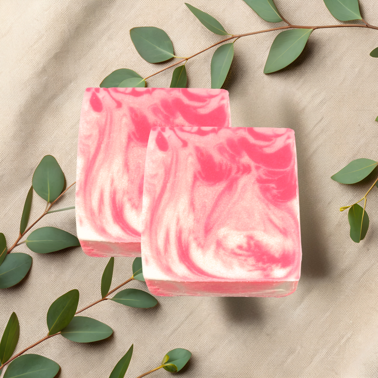 Two pink and white marbled soap bars on a beige fabric background with green leaves.