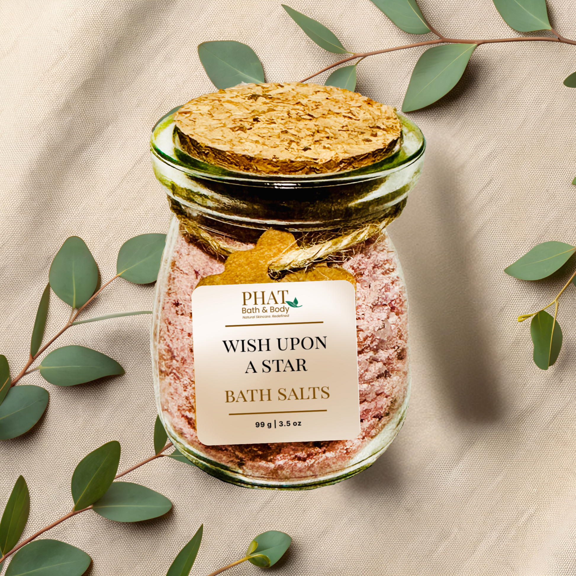 Jar of wish upon a star bath salts with a cork lid on a beige fabric background with eucalyptus leaves.