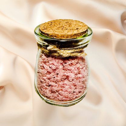 Small glass jar with cork lid containing bath salts on a beige fabric background.